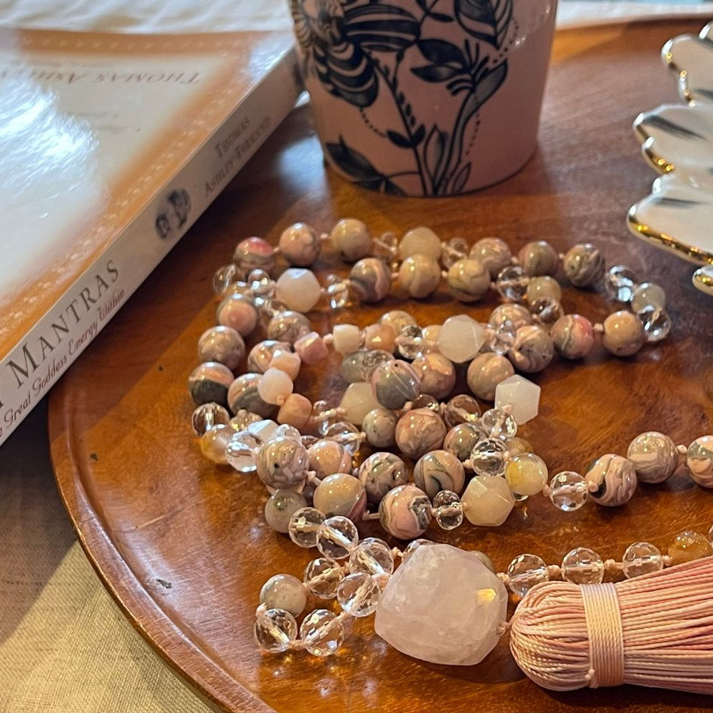 Necklace with beads and tassel on a wooden surface with a book and decorative items.