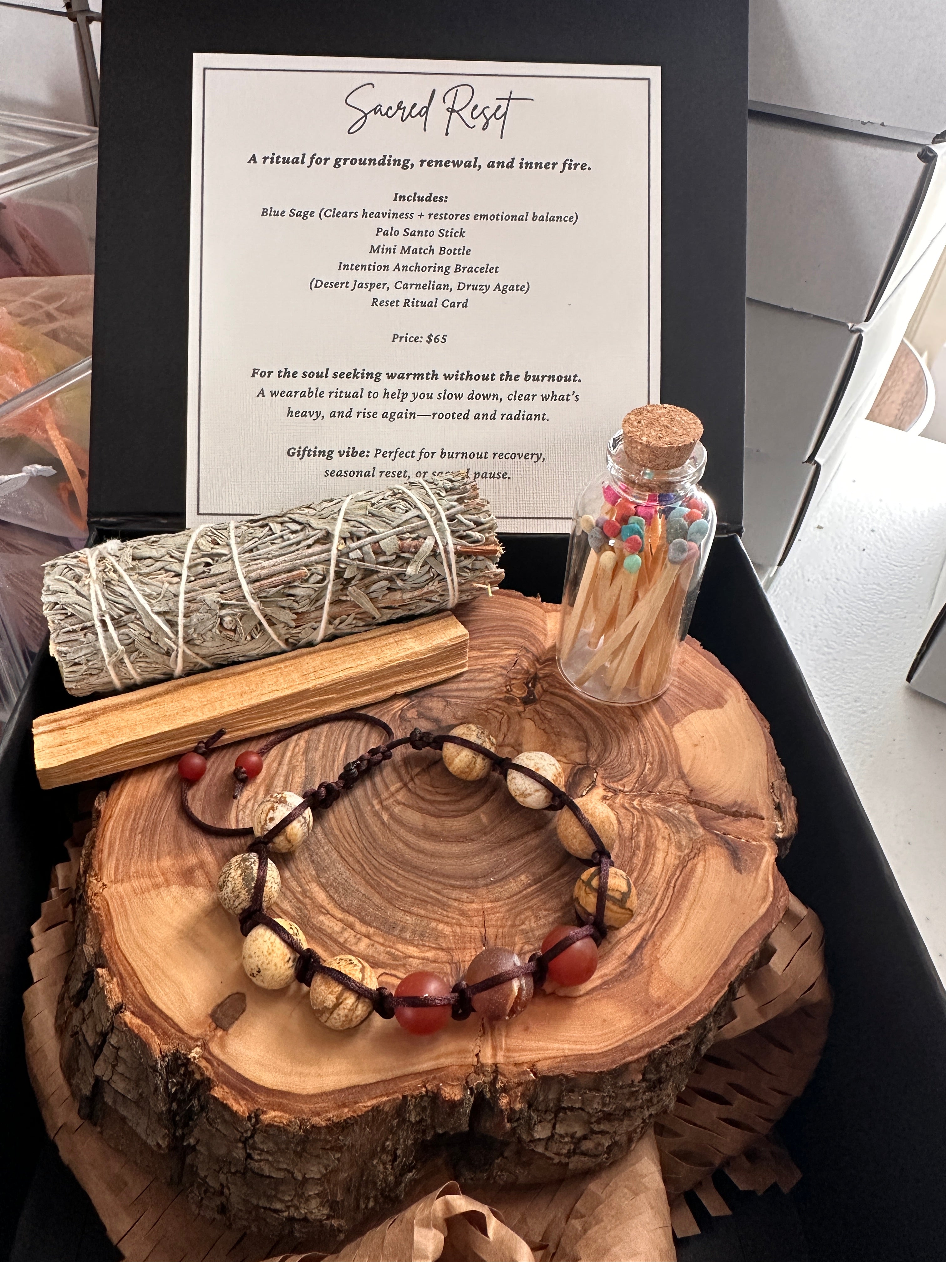 Wooden log with spiritual items including a bottle, sage, and bracelet on a table.